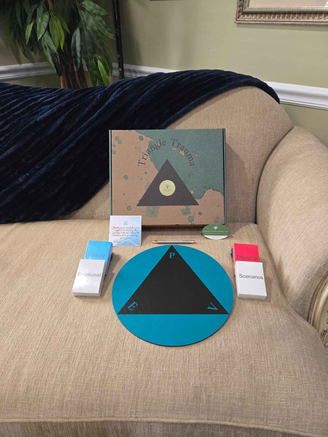 Trauma Triangle Display Board game setup featuring a triangle board, cards, and a map on a couch.